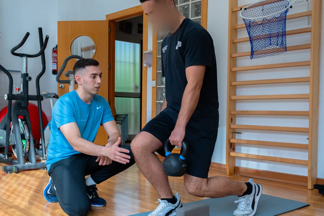 Alejandro Lozano, entrenador personal a domicilio en Málaga, corrigiendo de rodillas la zancada de un cliente con kettlebell