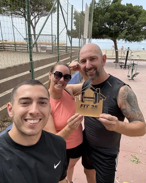 Dos clientes con su placa FIT 25 en una pista deportiva junto al mar